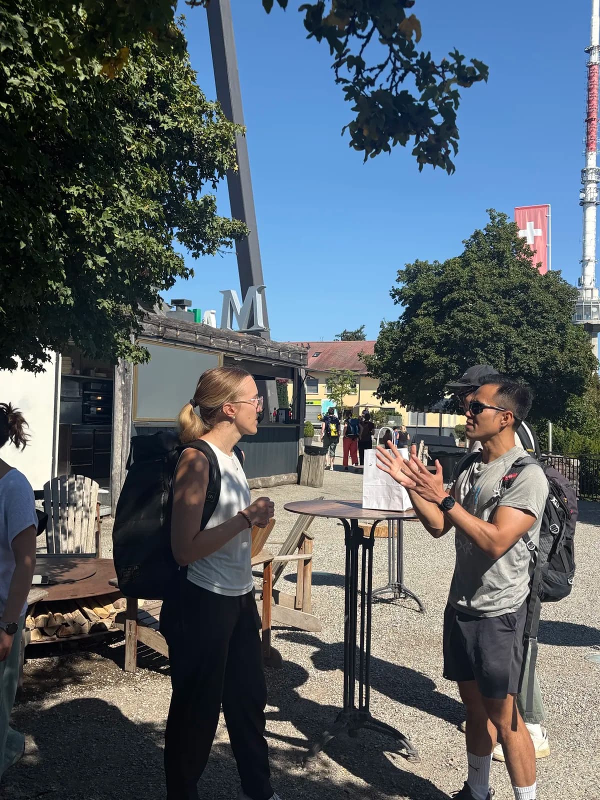 Participants in conversation during the morning hike on Uetliberg, with the Swiss flag and TV tower behind